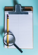 Notepad with pencil and magnifying glass on isolated background. Note book with magnifying glass