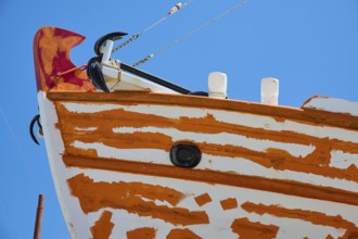 Close-up of the bow of a sailboat with orange and white paint and anchor in front of a blue sky,