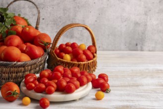 Fresh large and small tomatoes in baskets and on a white platter on a wooden table