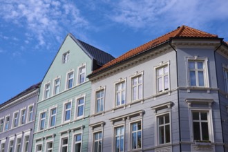 Several old buildings with different facade colours and red roof tiles in front of a blue sky with