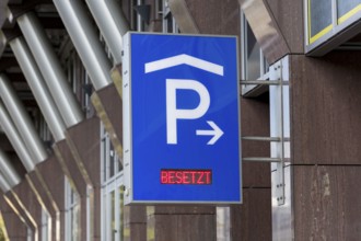 Blue car park sign with white P symbol and red display with the words 'Occupied' in front of modern