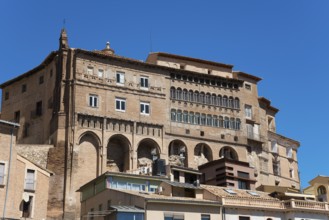 Large historic stone building with several windows and balconies under a clear blue sky, episcopal