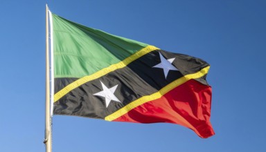 The flag of St Kitts, Caribbean, fluttering in the wind, isolated against a blue sky