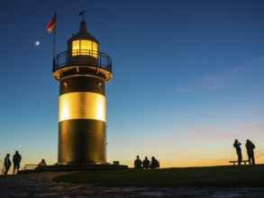 Black and white lighthouse, called 'Kleiner Preuße', illuminated at dusk with a clear blue sky, a