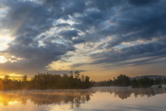 Fog over the lake at sunrise, dramatic clouds and reflecting water surface in natural surroundings,