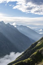 Atmospheric mountain landscape, sunbeams fall between peaks into a mountain valley, evening light,