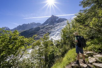 Hiker on hiking trail La Jonction, view of glacier Glacier des Bossons with sun star, behind summit