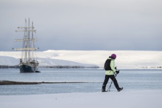 Woman with backpack and warm clothes on a snowy beach, in the background barkentine Antigua, winter