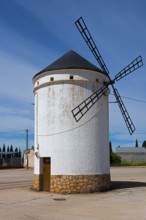 Small white windmill with blades and stone base under a clear sky, Mill, Molino de Villahermosa, La