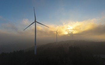 Wind turbines in a misty dawn with the sun behind clouds, Rems Valley, Baden-Württemberg, Germany,