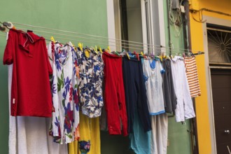 Men's and women's washed clothes drying on clothesline of green painted with white trim stucco