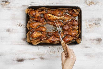 A hand holds a fork to serve crispy baked chicken drumsticks arranged on a tray. The setup is on a