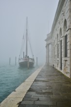 View from 'Fondamenta Salute' on an old sailing boat lying in the water in Venice on a foggy day in