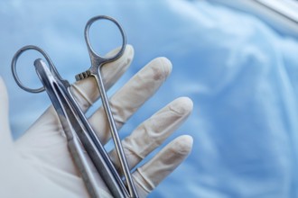 Gloved hand holding forceps with a blue background, indicating surgery preparation