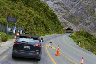 A car standing in front of a red light at a tunnel opening, surrounded by forest and mountains and