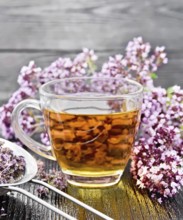 Oregano herbal tea in a glass cup, fresh flowers and metal strainer with dried marjoram flowers on