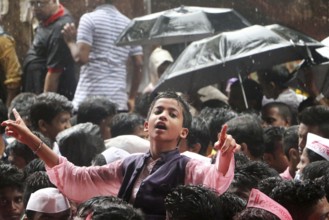 A boy braves the rain dances procession leading a gigantic idol of Hindu god Ganesh immersion