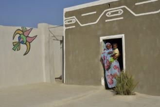 Woman carrying toddler, colorful painted Nubian house in the village Umogaal in Dongola, Nubia,