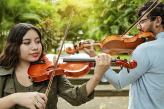 Violinist man and woman back to back playing violin in a park outdoors. Two young violinists