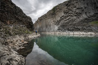 Tourist standing by the river in Stuðlagil Canyon, turquoise blue river between basalt columns,