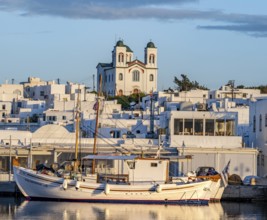 Fishing boats in the harbour at sunset, reflected in the sea, White Cycladic houses and church