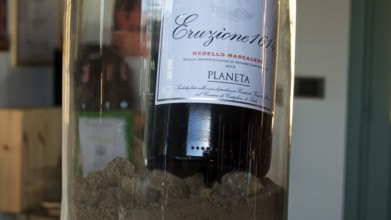 Wine bottle in a glass container presented on sand, focus on label, Planeta winery, Sicilian wine,