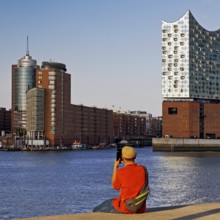 A man takes pictures of the Elbe Philharmonic Hall and Columbus House, Hafencity, Hamburg, Germany,