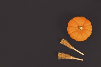 Orange Halloween pumpkin and witch brooms in corner of black background with copy space