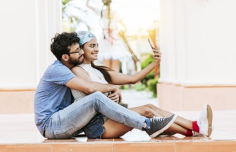 Young couple taking a selfie sitting on the floor. Young latin couple in love sitting on the floor