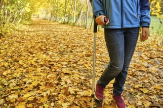 Young teenage girl walks with crutch through colourful autumn leaves