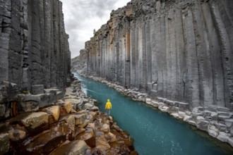 Tourist standing by the river in Stuðlagil Canyon, turquoise blue river between basalt columns,