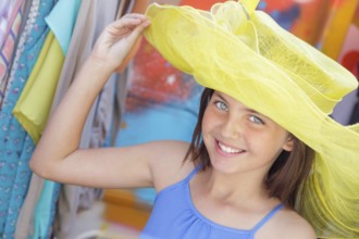 Cute blue eyed girl playfully modeling a big sun hat at the market