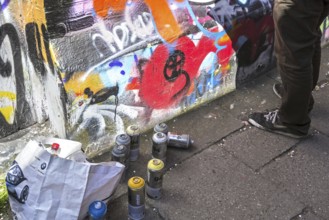 Spray cans and younster spraying colourful graffiti on wall in alley