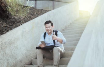 Young man sitting on stairs with cell phone and thumb up, Smiling guy sitting on stairs with cell