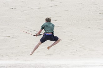 Young man handling 4 line control bar of a flying quad lines trainer parafoil, 4 line stunt kite on