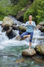 Woman in Hatha yoga balance yoga asana Vrikshasana tree pose at waterfall outdoors