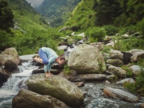 Woman doing Kakasana asana, crow pose arm balance outdoors at tropical waterfall. Vintage retro