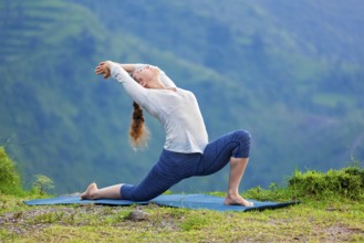 Yoga outdoors, sporty fit woman practices Hatha yoga asana Anjaneyasana, low crescent lunge pose