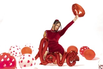 Beautiful elegant girl in red dress surrounded by balloons on white background with love sign.