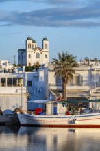 Fishing boats in the harbour at sunset, reflected in the sea, White Cycladic houses and church