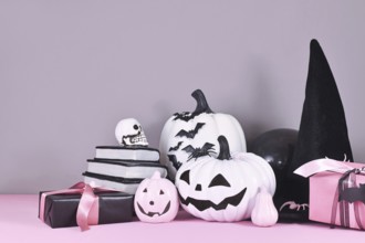 Pink and white Halloween decor with black and white pumpkins, witch hat and spell books on gray