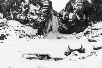 Frozen waterfall, Folaldafoss, snowy rock face and snowy landscape, black and white photo,