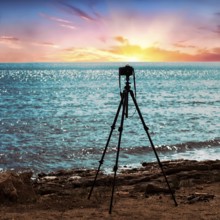 Tripod with camera stands on the beach, colourful sunset by the sea, backlighting