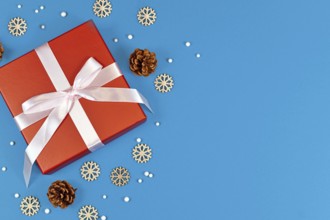 Red Christmas gift box with ribbon surrounded by seasonal pine cones and wooden snowflake ornaments