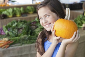 Happy young blue eyed girl holding a fresh pumpkin at the farmers market