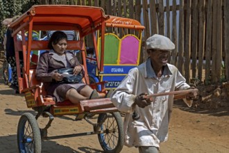 Old Malagasy man pulling pousse-pousse, pulled rickshaw with local woman in the city Antsirabe,