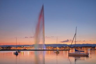 The Jet d'eau at dusk is the landmark in Geneva's harbour basin, with sailboats in the foreground