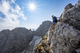 Mountaineer on a rocky narrow mountain path, view of rock faces with blue ice glacier and summit of