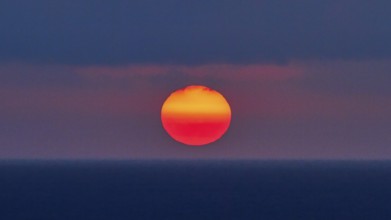 Sun as a fiery red big ball, blue-purple sky, sun just above the horizon, sunset, evening light,