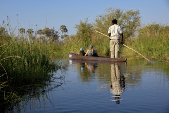 Tourists in a mokoro or dugout boat on safari in swamp area, Gomoti Plains Camp, Gomoti Concession